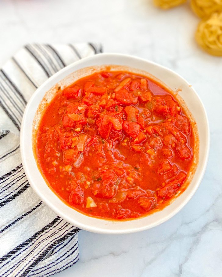 Gęsty domowy sos marinara w ceramicznej miseczce udekorowany świeżą bazylią.